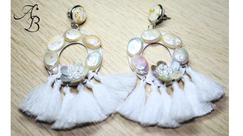Boucles d'oreilles en forme de cercle avec des perles nacrées et pampilles blanches, sur fond en bois clair.