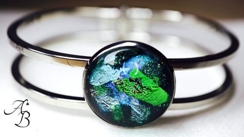 Bracelet cabochon en acier avec un cabochon en verre aux teintes vertes et bleues.