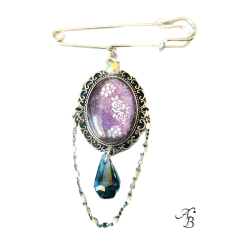 Broche – Floraison améthyste avec cabochon violet fleuri, cristal suspendu et double chaîne décorative.