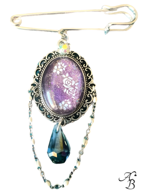 Broche – Floraison améthyste avec cabochon violet fleuri, cristal suspendu et double chaîne décorative.