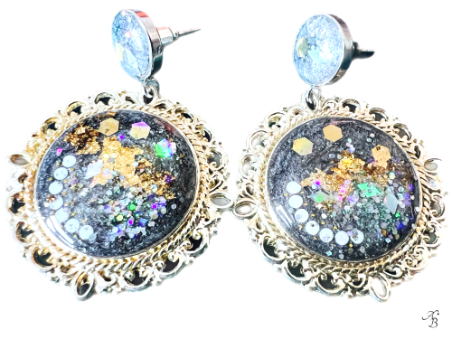 Boucles d’oreilles clous Terre australe avec cabochon noir et paillettes holographiques, reflets multicolores et touches dorées.
