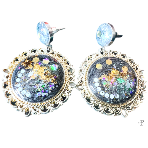 Boucles d’oreilles clous Terre australe avec cabochon noir et paillettes holographiques, reflets multicolores et touches dorées.