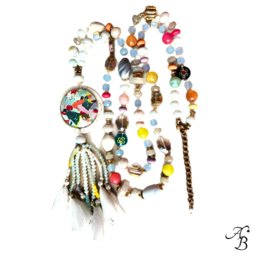 Sautoir Atelier bohème composé de perles multicolores en cristal et pierres naturelles, pendentif en pierre avec cabochon de verre et pompons blancs.