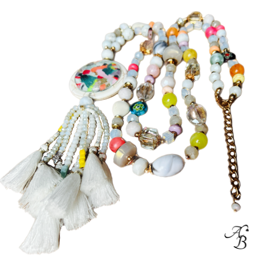 Sautoir Atelier bohème composé de perles multicolores en cristal et pierres naturelles, pendentif en pierre avec cabochon de verre et pompons blancs.