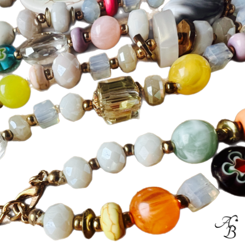 Sautoir Atelier bohème composé de perles multicolores en cristal et pierres naturelles, pendentif en pierre avec cabochon de verre et pompons blancs.