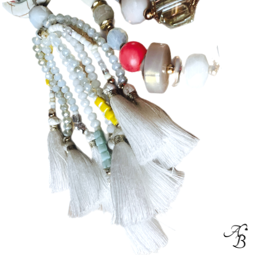 Sautoir Atelier bohème composé de perles multicolores en cristal et pierres naturelles, pendentif en pierre avec cabochon de verre et pompons blancs.