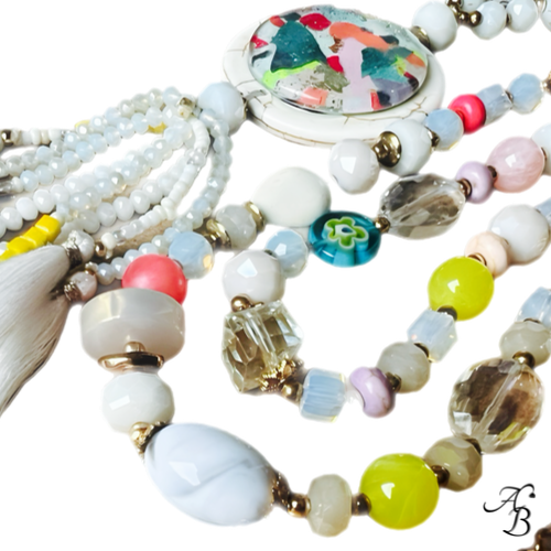 Sautoir Atelier bohème composé de perles multicolores en cristal et pierres naturelles, pendentif en pierre avec cabochon de verre et pompons blancs.