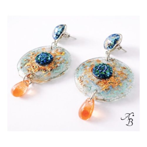 Boucles d’oreilles clous Resin’ Myosotis en résine transparente avec feuilles métalliques, paillettes holographiques, cabochon bleu effet AB et goutte verre orangé - Aline B Création.